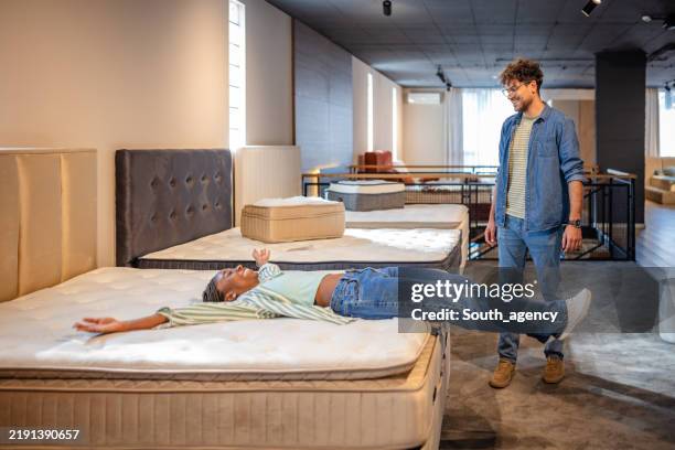a woman playfully tests comfort on a showroom mattress. - mattress stock pictures, royalty-free photos & images