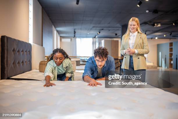 young couple examining mattress texture in showroom. - matras stockfoto's en -beelden