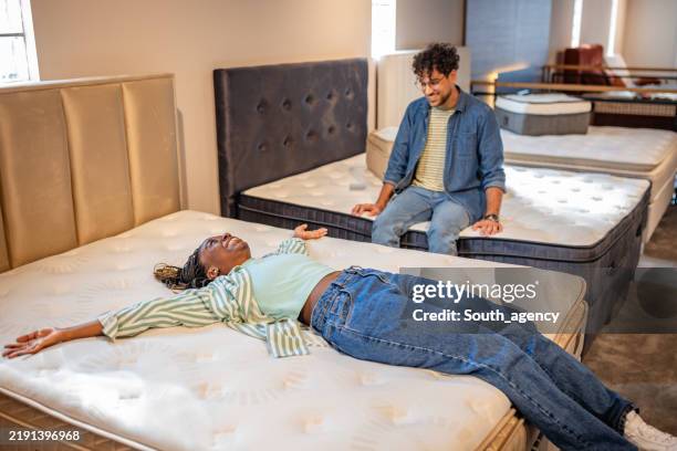 two people enjoying mattress testing in bright showroom. - matras stockfoto's en -beelden