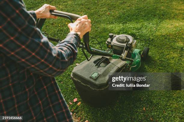 senior woman mowing the lawn in a rustic garden setting - cortar relva imagens e fotografias de stock