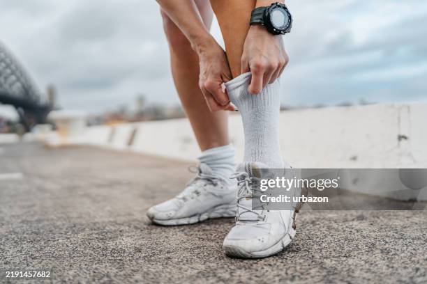 mid-adult chinese woman pulling up her socks before jogging near the sydney harbor bridge in sidney in australia - sock stock pictures, royalty-free photos & images