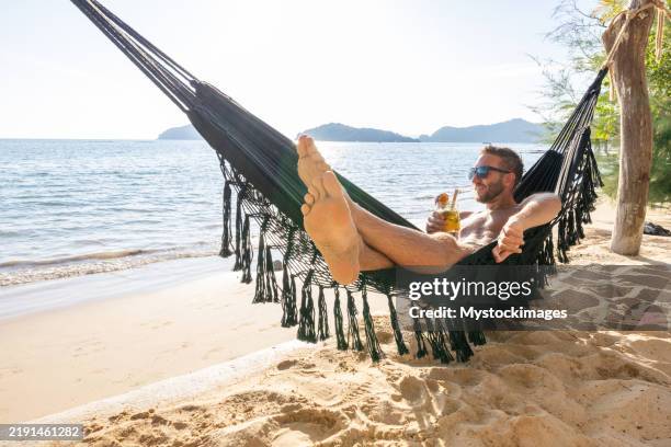 hombre relajándose en hamaca con bebida en la playa tropical - un solo hombre fotografías e imágenes de stock
