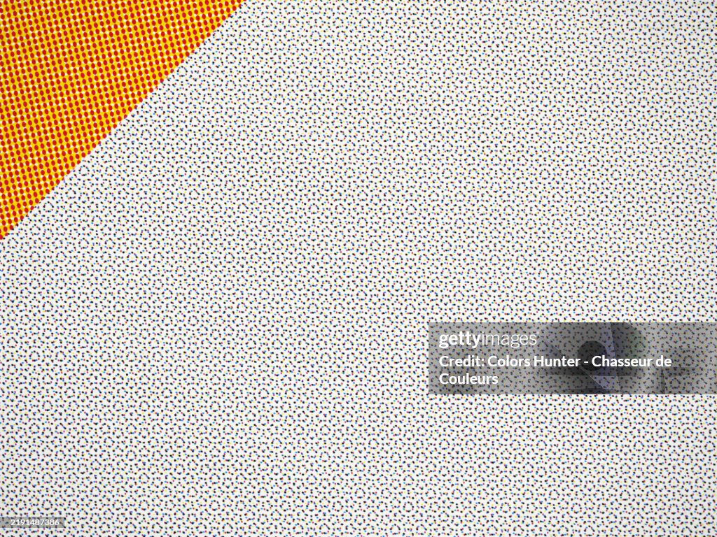 Macro photography of an offset printed poster: colored dots on a white background with a yellow and red corner. Natural light and colors. Paris, France.
