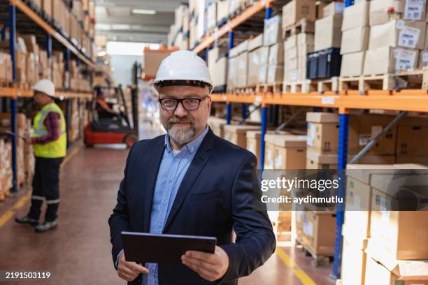 gestión eficiente de la fábrica: retrato del hombre de negocios o del director general sonriente que utiliza la tableta para supervisar la producción en el almacén de la fábrica industrial. - casco de trabajo fotografías e imágenes de stock