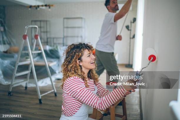 glückliches paar malte eine wand mit einem paint roller - dekorieren stock-fotos und bilder