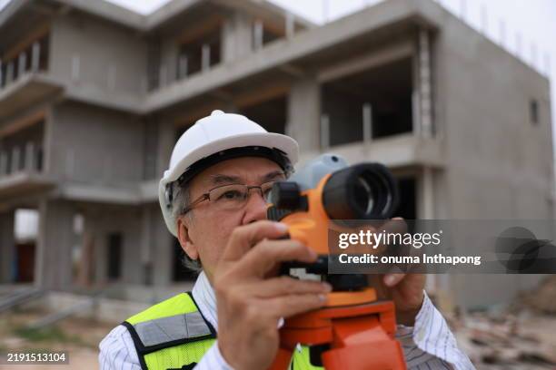 a senior construction male engineer working with the theodolite camera at the housing under construction - tacheometer stock pictures, royalty-free photos & images