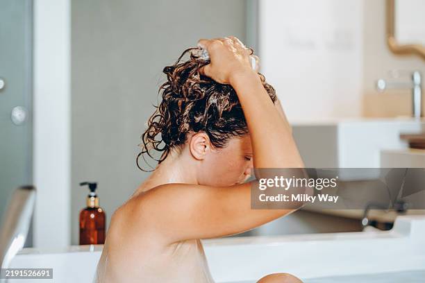 beautiful young woman taking a hot bath and washing long hair with foam shampoo. - cuero cabelludo fotografías e imágenes de stock