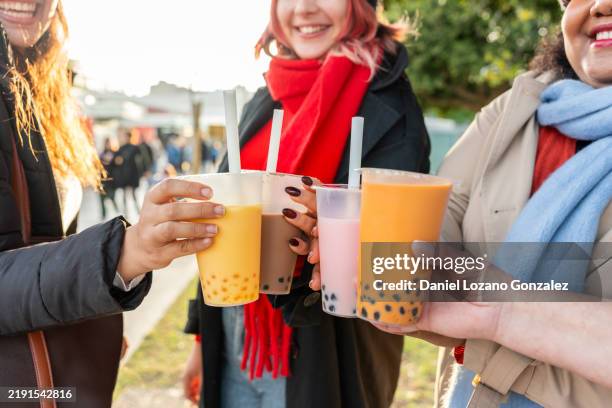 three friends are toasting with bubble tea at a street food market - bubble tea stock pictures, royalty-free photos & images