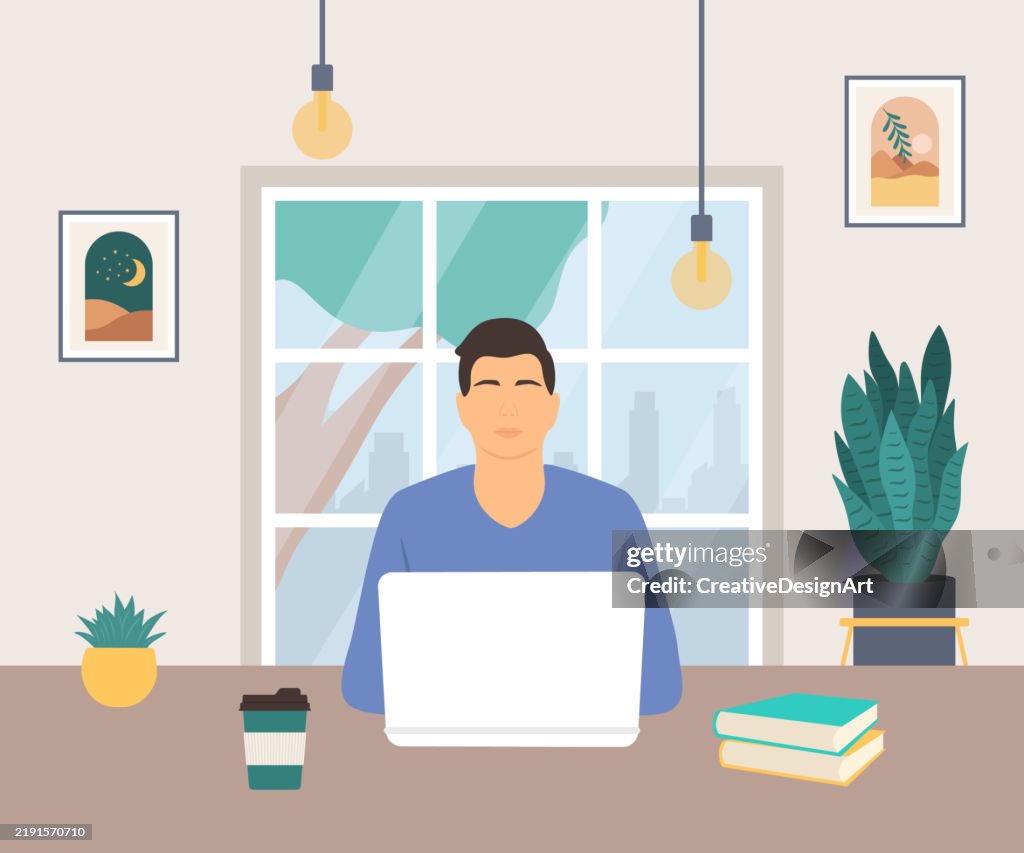 Young Man Working On Laptop In Cafe. Modern Cafe Interior With Picture Frames On The Wall, Potted Plant And Pendant Lights