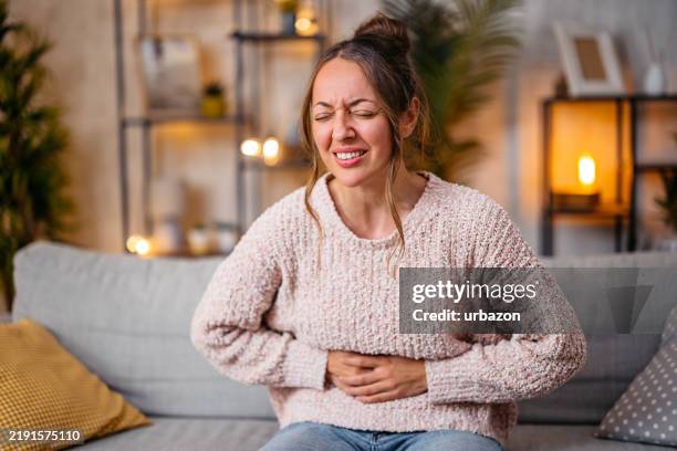 frau im mittleren erwachsenenalter, die zu hause bauchschmerzen hat - zyklus stock-fotos und bilder