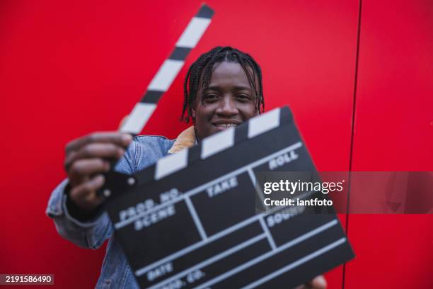 young filmmaker smiling and holding a clapperboard on red background. - scenario stockfoto's en -beelden
