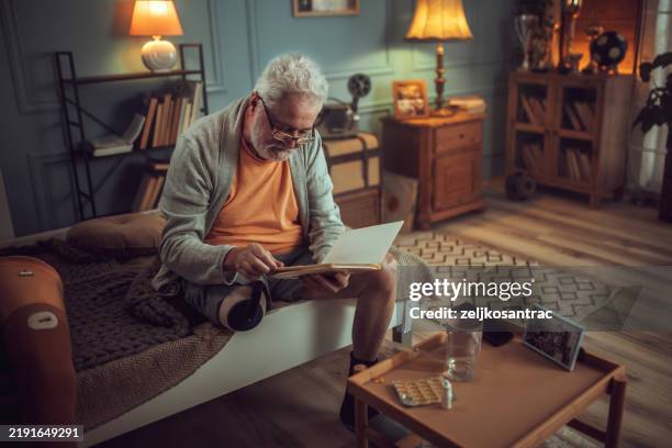 senior man with a disability looks at his photo album and reminisces about the past - looking at old photo stock pictures, royalty-free photos & images