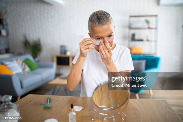 woman applying hydrogel under-eye patches at home, enhancing her skincare routine with beauty treatment - eye patch stock pictures, royalty-free photos & images