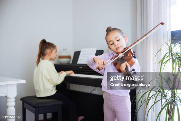 zwei schwestern haben spaß daran, gemeinsam klavier und geige zu üben - musikalische begleitung stock-fotos und bilder