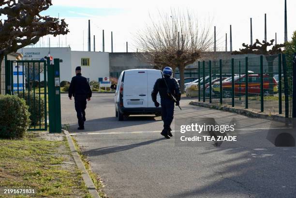 Police officers stand next to a car at the entrance gate during a hostage situation inside the Arles prison in Arles, southern France, on January 3...
