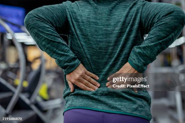 painful moment: woman holding her back during gym session - lower back stock pictures, royalty-free photos & images