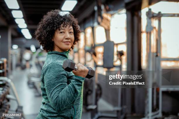 confident woman smiling at the camera in a modern gym setting - tyngdlyftning bildbanksfoton och bilder