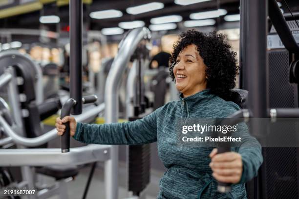strong and determined: mature woman exercising in the gym - exercise machine stock pictures, royalty-free photos & images