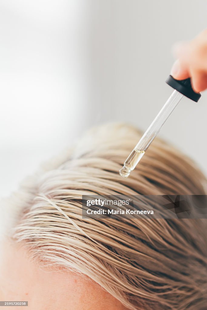 Woman applies oil to her hair with pipette.