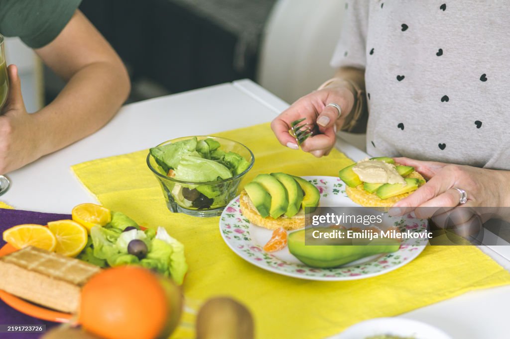 Mother and son enjoying in preparation of a healthy breakfast in the morning at home. Superfoods ingredients for first meal of the day spirulina, smoked tofu, avocado, lettuce, rice cakes, fruits.