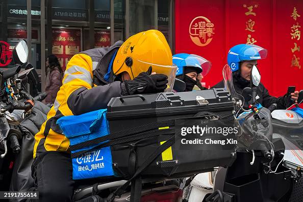 Chinese Delivery Riders A delivery rider wearing a Meituan uniform leans on their motorbike ...