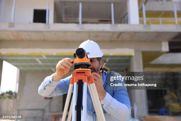 surveyor with walkie-talkie looking through measuring level on construction site - tacheometer stock pictures, royalty-free photos & images