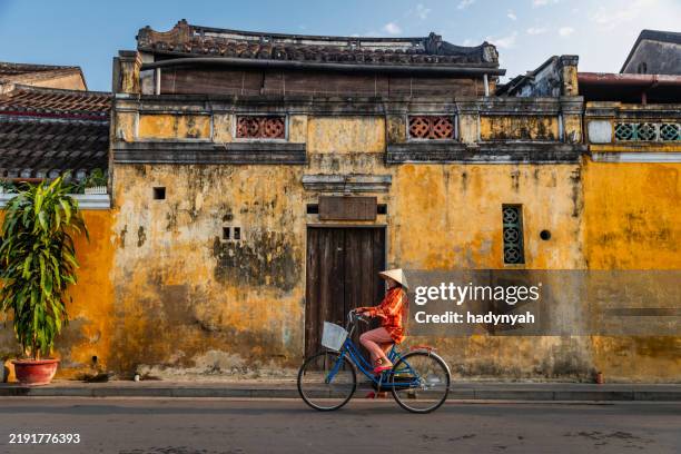 vietnamese woman rides a bicycle in an old town of hoi an city, vietnam - hoi an stockfoto's en -beelden