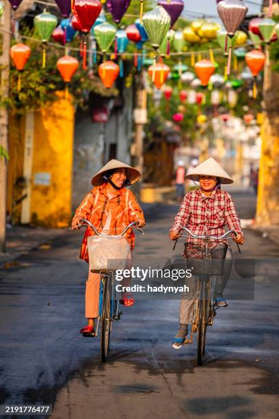 vietnamese women ride bikes in an old town of hoi an city, vietnam - cultura vietnamita imagens e fotografias de stock