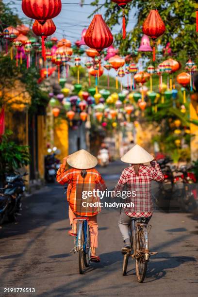 vietnamese women ride bikes in an old town of hoi an city, vietnam - hoi an stockfoto's en -beelden