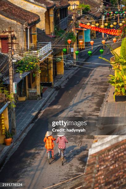 vietnamese women ride bikes in an old town of hoi an city, vietnam - hoi an stockfoto's en -beelden