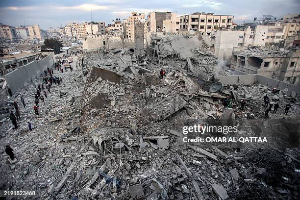 People and first responders inspect the rubble of a collapsed residential building that was hit by Israeli bombardment in the Saraya area in al-Rimal...