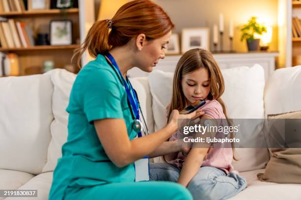 nurse assisting young girl with glucose monitor during routine healthcare check - glycemia stock pictures, royalty-free photos & images