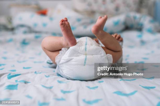 view of a baby lying in bed. feet up and diaper. - pañal fotografías e imágenes de stock