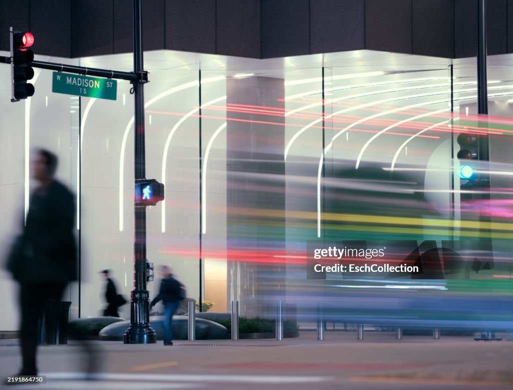 Early morning image with business people and traffic passing illuminated office facade