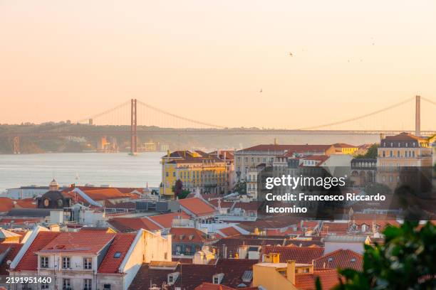 lisbon, rooftops and bridge at sunset - lissabon stockfoto's en -beelden