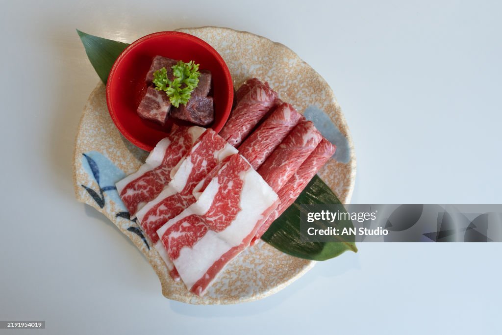 Premium rare slices wagyu A5 beef with high marbled texture on square wooden plate served for sukiyaki and shabu.