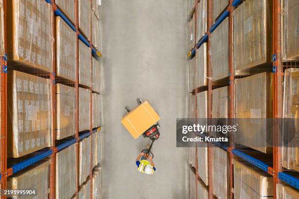 high angle view of male warehouse worker of warehouse worker moving pallet of goods with pallet truck at distribution warehouse. - warehouse worker stock pictures, royalty-free photos & images