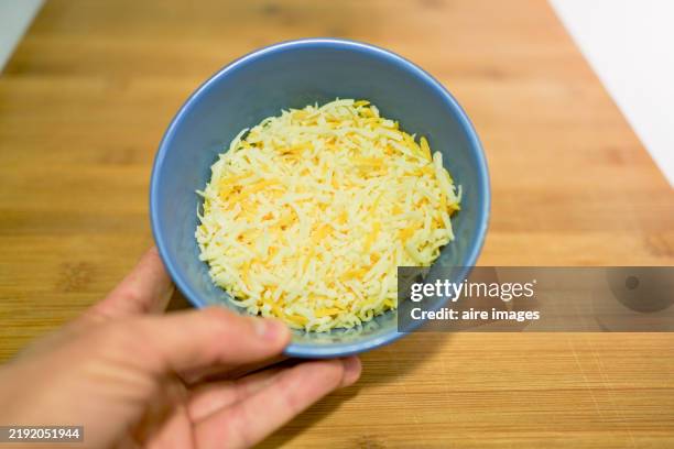 close-up front view of a bowl of yellow striped cheese held by a human hand on a table - grated stock pictures, royalty-free photos & images