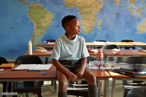 schoolboy looking away while sitting on desk - zuidelijk afrika stockfoto's en -beelden