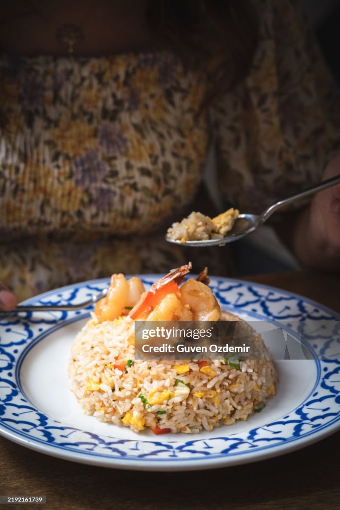 Primer plano de arroz tailandés frito con huevo y gambas, servido en un plato tradicional azul y blanco en un restaurante tailandés