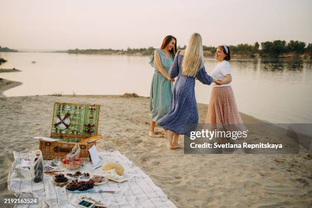 three women holding hands and spinning on a riverbank at sunset during a picnic - riverside california stock pictures, royalty-free photos & images