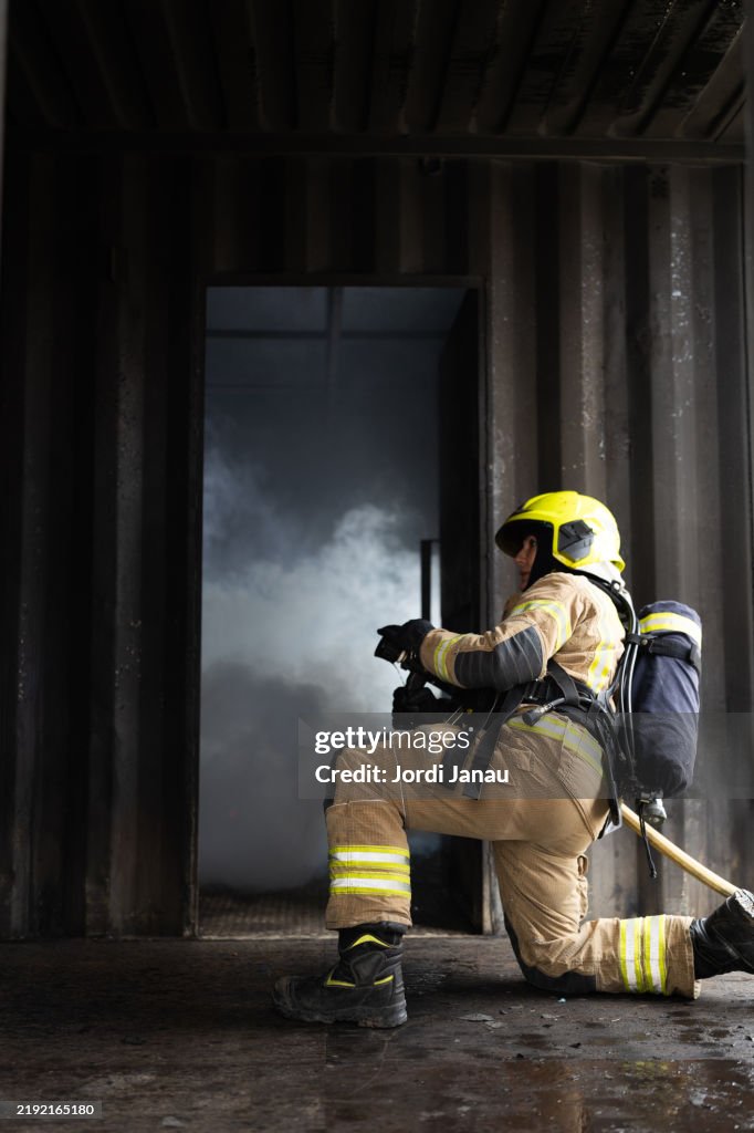 Female firefighter kneeling and holding a fire hose during a fire drill