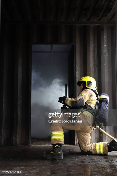 female firefighter kneeling and holding a fire hose during a fire drill - feuerwehrschlauch stock-fotos und bilder