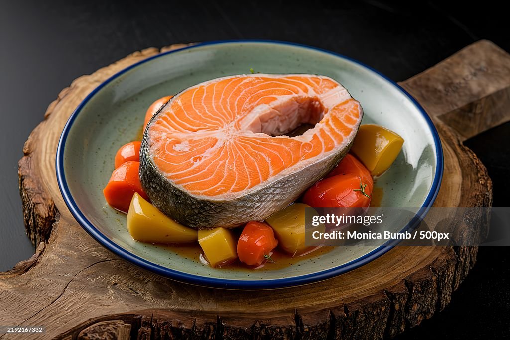 A salmon steak on a pillow of stewed vegetables on a plate