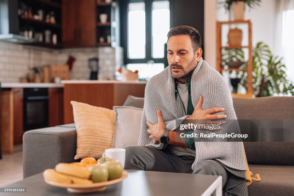 Sick man shivering under blanket on sofa at home