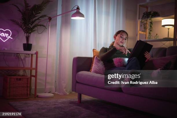 giovane donna che si rilassa sul divano, mangiando popcorn e guardando film su tablet di notte - video on demand foto e immagini stock