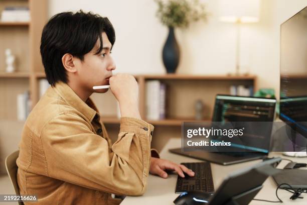 focused programmer analyzing code on dual monitors in modern workspace - software programmer stock pictures, royalty-free photos & images