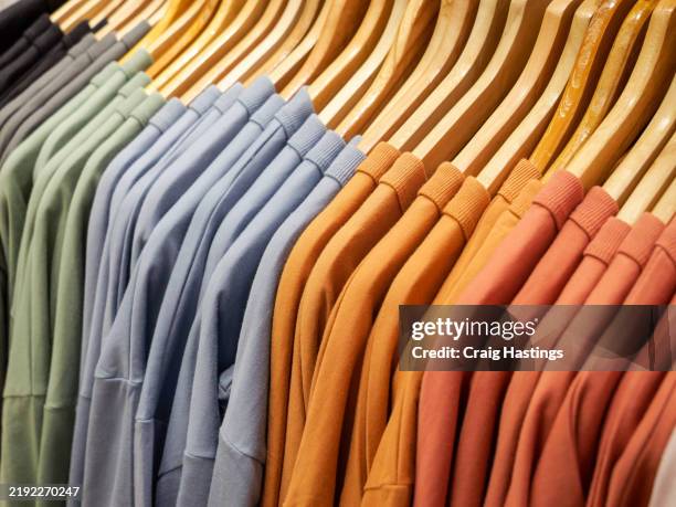 close up of stack of t-shirts on hangers and racks in department store in london, uk. plain standard style shirts in original stone wash and earthy colours and patterns - fast fashion stock pictures, royalty-free photos & images