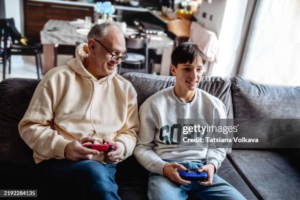 father and son playing video games on a sofa. happy expressions. family leisure time captured. great for lifestyle, family, or gaming themes. - foster care stock pictures, royalty-free photos & images