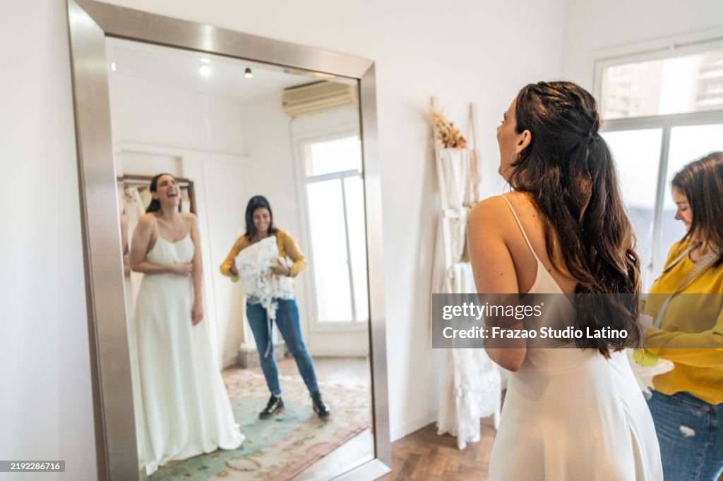 Sposa che prova l'abito da sposa con l'aiuto della commessa in un negozio di abiti da sposa